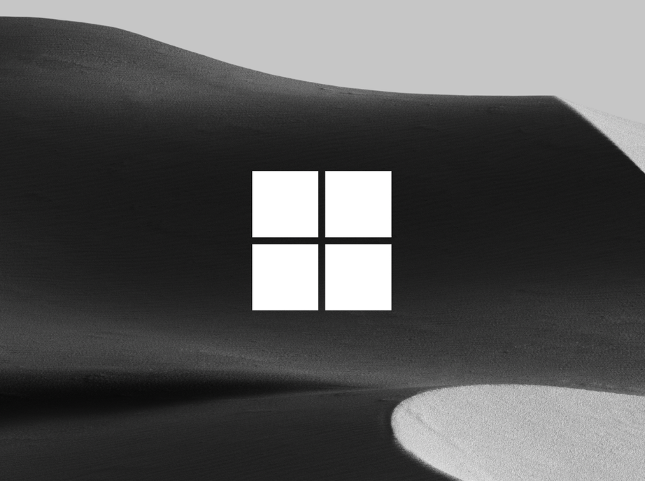 Microsoft logo in white over a dark sand dune in black and white.
