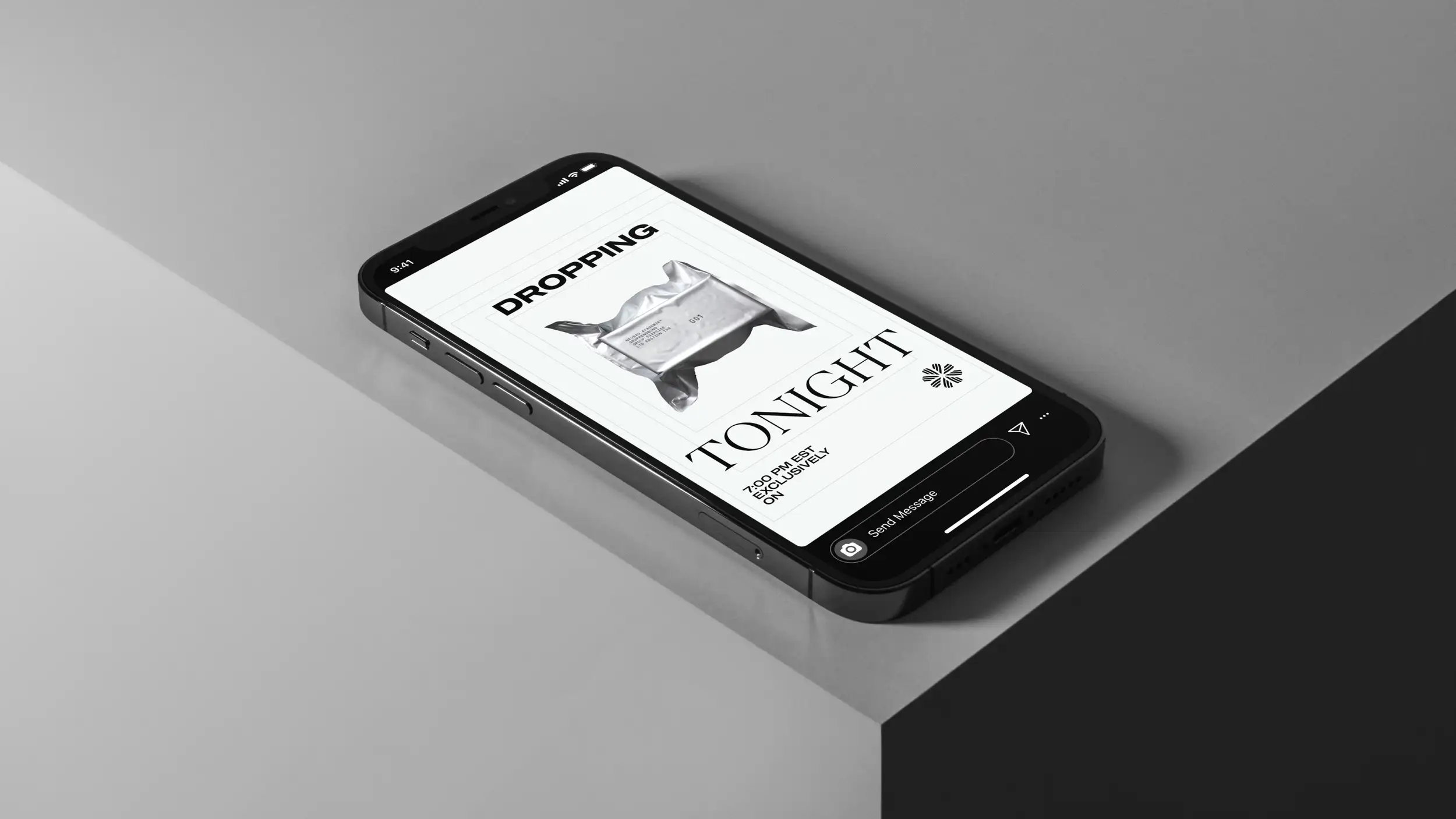 A black smartphone lying on the edge of a light gray surface at an angle, displaying an Everbloom social-media story in portrait orientation. The status bar reads 9:41. The story is set on a white background with bold black text reading "DROPPING" at the top and "TONIGHT" in large serif type lower down, framing a photo of a silver foil-wrapped package or product. Smaller text reads "7:00 PM EST EXCLUSIVELY ON" beside the Everbloom floral logo. An Instagram-style "Send Message" bar with camera, share, and more icons sits at the bottom of the screen.