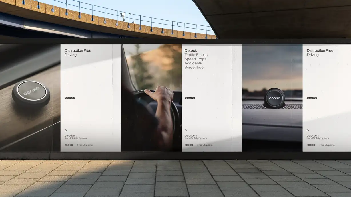 Wide outdoor billboard mounted beneath a concrete overpass. Three product panels advertise the OOONO Co-Driver 1 Road Safety System (49.99€, free shipping): a close-up of the black circular device, a driver's hand on a steering wheel, and the device mounted on a car dashboard. Text reads "Distraction Free Driving" and "Detect: Traffic Blocks. Speed Traps. Accidents. Screenfree."