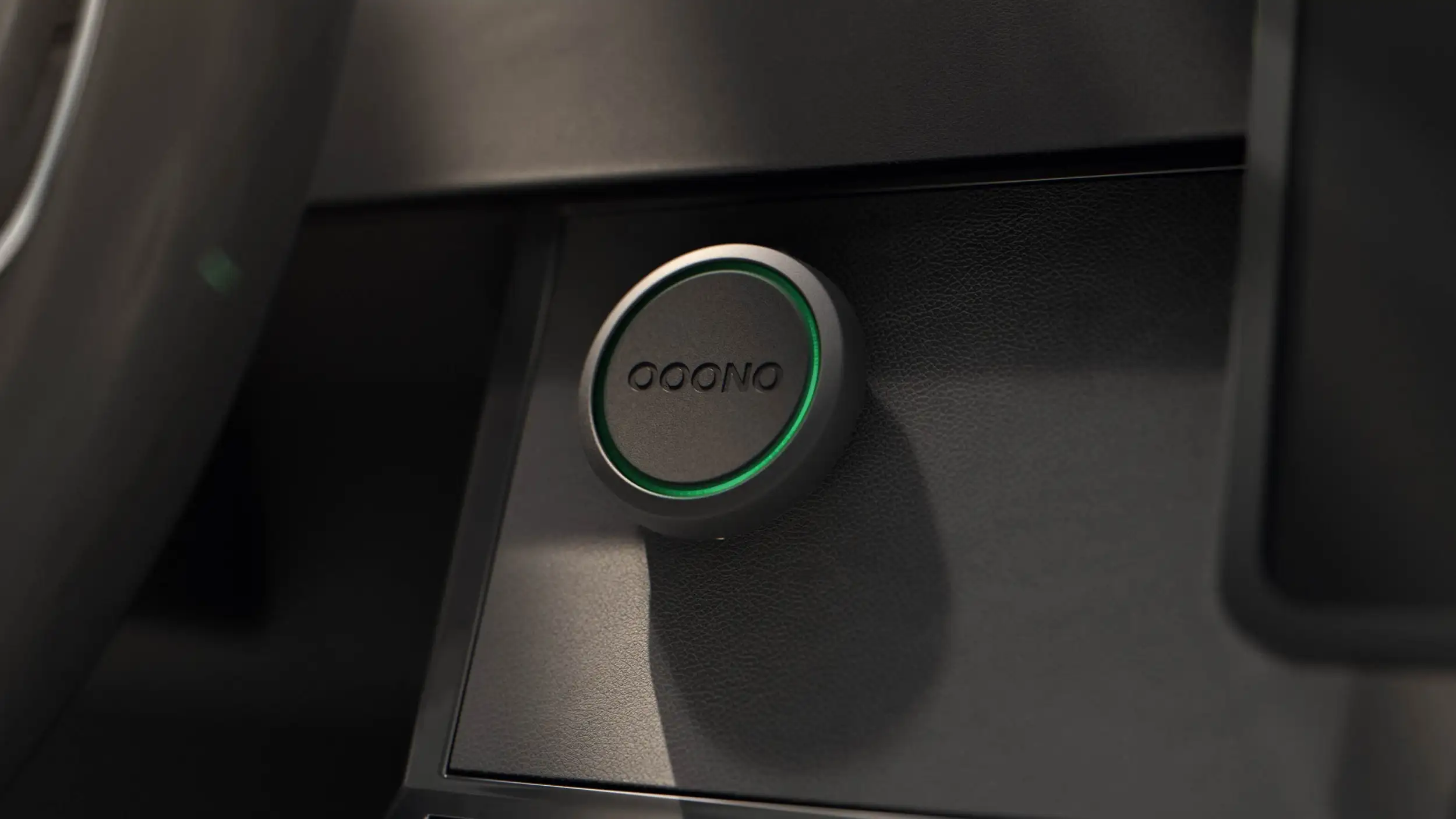Close-up of a round device mounted on a car dashboard, labeled "Ooono," with a green LED ring around its edge.