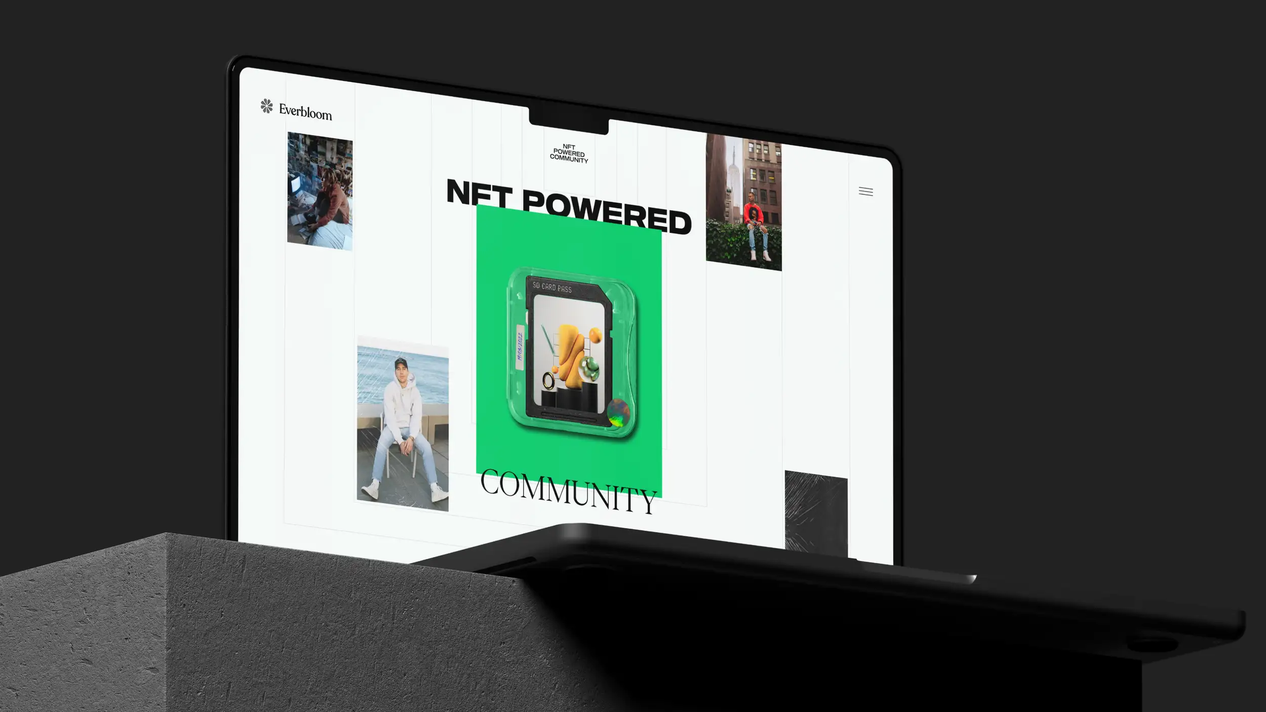 A laptop shown at a dramatic angle, resting on a dark textured concrete block against a black background, displaying the Everbloom website homepage. The "Everbloom" logo sits in the top-left corner and a hamburger menu in the top-right. The large headline reads "NFT POWERED" at the top and "COMMUNITY" in serif type below, framing a bright green central tile that features a 3D render of an "SD Card Pass" containing abstract colorful objects. Surrounding lifestyle photos show young people in casual streetwear — one seated by the sea in a white hoodie, one at a desk, and one in a red top seated against a New York City backdrop with the Empire State Building visible.