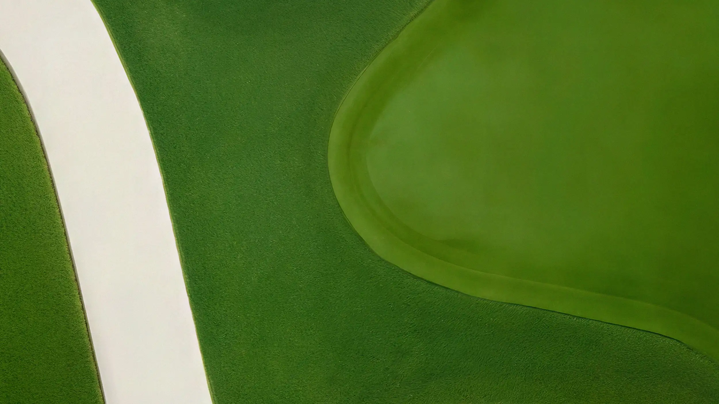 Aerial view of a golf course showing a curved white sand bunker beside a smooth oval putting green.