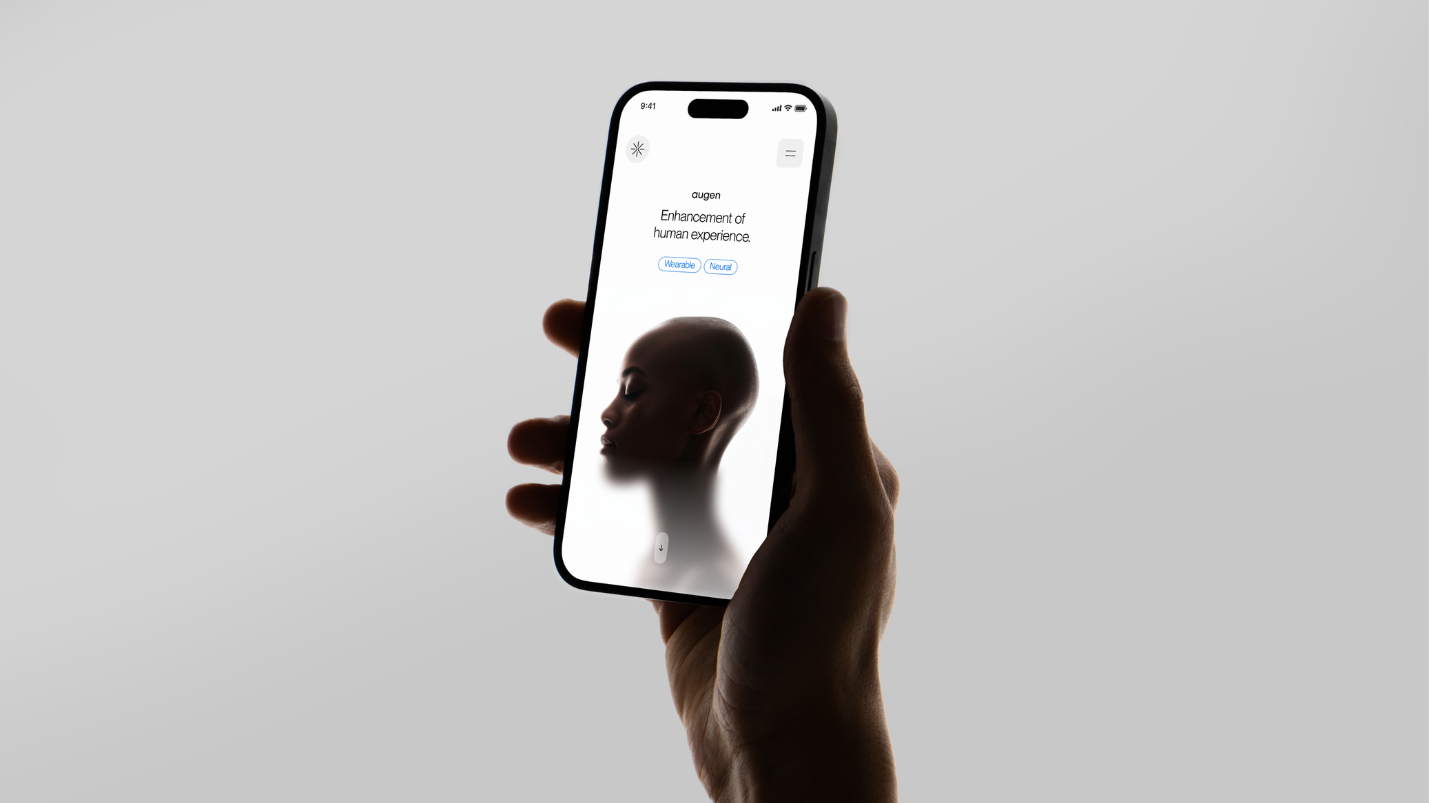 A hand holds up a smartphone against a plain light gray background, displaying the mobile homepage of the Augen website. The status bar reads 9:41 with full signal, Wi-Fi, and battery. The starburst logo sits in the top-left corner and a hamburger menu button in the top-right. Centered text shows the "augen" wordmark above the headline "Enhancement of human experience.", with two blue pill buttons labeled "Wearable" and "Neural" beneath it. Below, a softly lit portrait photo shows the profile of a bald person with eyes closed, fading into a bright white background. A downward-arrow scroll button appears near the bottom of the screen.