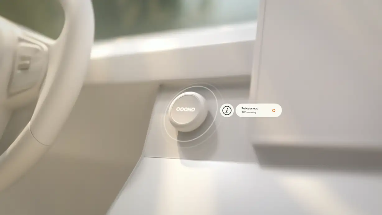 A softly lit, all-white minimalist car interior rendered in a monochrome cream palette, with a blurred steering wheel on the left and a dashboard screen on the right. In the center, a white circular OOONO Co-Driver device sits mounted on the dashboard, emitting concentric ripple rings to suggest it is actively signaling. To its right, a floating white notification pill with an "i" information icon reads "Police ahead — 100m away," accompanied by a small orange circular OOONO marker. Green foliage is faintly visible through the window in the background.
