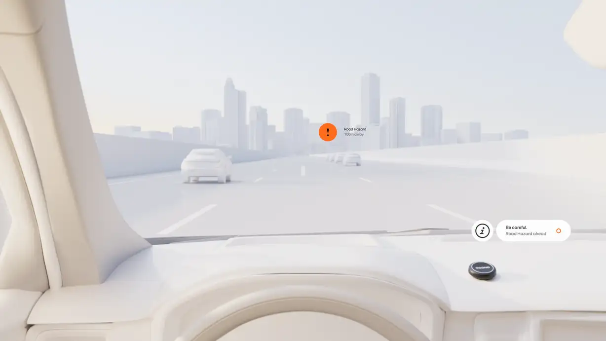 A driver's-eye view through the windshield of an all-white, minimalist car interior, looking out onto a highway rendered in the same monochrome cream palette. Simplified white cars drive ahead on the multi-lane road, with a stylized city skyline of skyscrapers on the horizon under a pale sky. An orange circular alert badge with an exclamation mark floats over the road, labeled "Road Hazard — 100m away." In the lower right, a floating white notification pill with an "i" information icon reads "Be careful. Road Hazard ahead," next to a small orange OOONO marker. The black OOONO Co-Driver device sits mounted on the dashboard in the bottom-right corner.