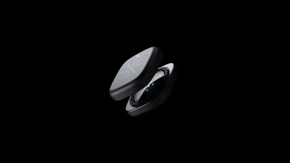 A dramatic product render of the Augen A¹ Sense wearable device floating against a pure black background. The small, rounded square device is shown split open into two halves: the upper half displays a matte dark-gray surface engraved with the Augen starburst logo and small regulatory markings (CE, IP68), while the lower half reveals the intricate internal components, including a ring of circuitry and several glowing blue LED indicator lights. Soft studio lighting highlights the device's smooth, pebble-like edges.