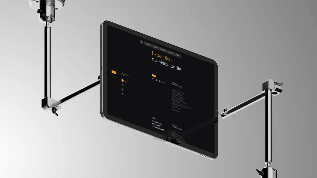 A tablet held horizontally in mid-air by two chrome articulated clamp arms that grip its left and right edges against a smooth gray gradient background, giving a technical, studio-rig look. The screen shows the Augen "B¹ Eye" technical-specifications page in near-black with amber-yellow accents. A dark navigation bar sits near the top (starburst logo; menu links Wearable, Neural, Programs, Updates, Search), below the heading "Expanding our vision on life" (with "Expanding" in yellow). A left sidebar labeled "Development Of B¹ Eye" lists icon steps. The main content shows two spec blocks marked "Research & Development STAGE": "IoT Connectivity" (tag "IOTC") listing items like Communication Protocols, Network Topologies, Wearable Compatibility, Data Security, and Ethics & Safety; and "Autonomous AI-powered Personal Agent" (tag "APA") listing items like ASI-Based, Advanced Algorithms, Continuous Learning, Decision-Making Autonomy, and Reasoning & Problem Solving.