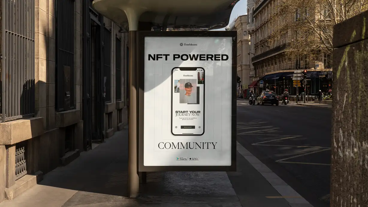A large Everbloom advertising poster displayed in a street-side bus shelter on a sunny European city street, likely Paris, with Haussmann-style stone buildings, sidewalk cafés, parked cars, and motorcyclists in the background. The white poster is headed with the "Everbloom" logo, the bold headline "NFT POWERED" at the top and "COMMUNITY" in elegant serif type at the bottom. At its center, a smartphone mockup displays the Everbloom app showing a person's profile/NFT card, with the call-to-action "START YOUR JOURNEY NOW — To get you started, we would like to gift you your first NFT" and a "Receive Free NFT" button. Google Play and App Store download badges appear near the bottom.