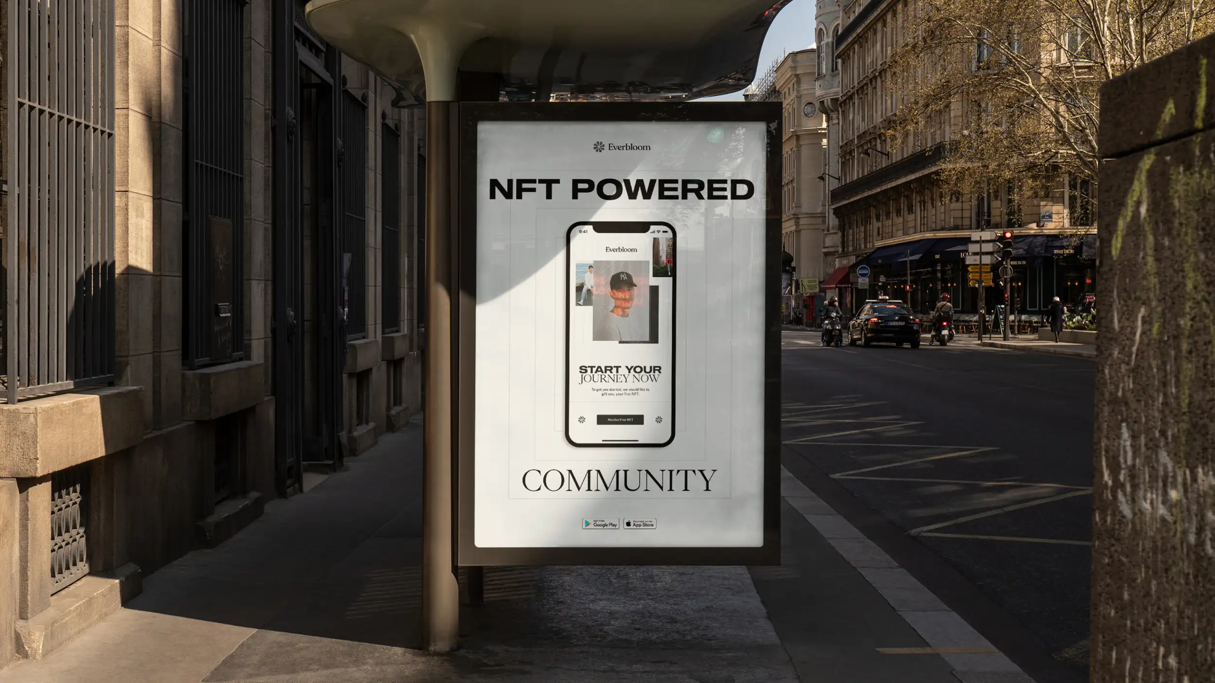 A large Everbloom advertising poster displayed in a street-side bus shelter on a sunny European city street, likely Paris, with Haussmann-style stone buildings, sidewalk cafés, parked cars, and motorcyclists in the background. The white poster is headed with the "Everbloom" logo, the bold headline "NFT POWERED" at the top and "COMMUNITY" in elegant serif type at the bottom. At its center, a smartphone mockup displays the Everbloom app showing a person's profile/NFT card, with the call-to-action "START YOUR JOURNEY NOW — To get you started, we would like to gift you your first NFT" and a "Receive Free NFT" button. Google Play and App Store download badges appear near the bottom.