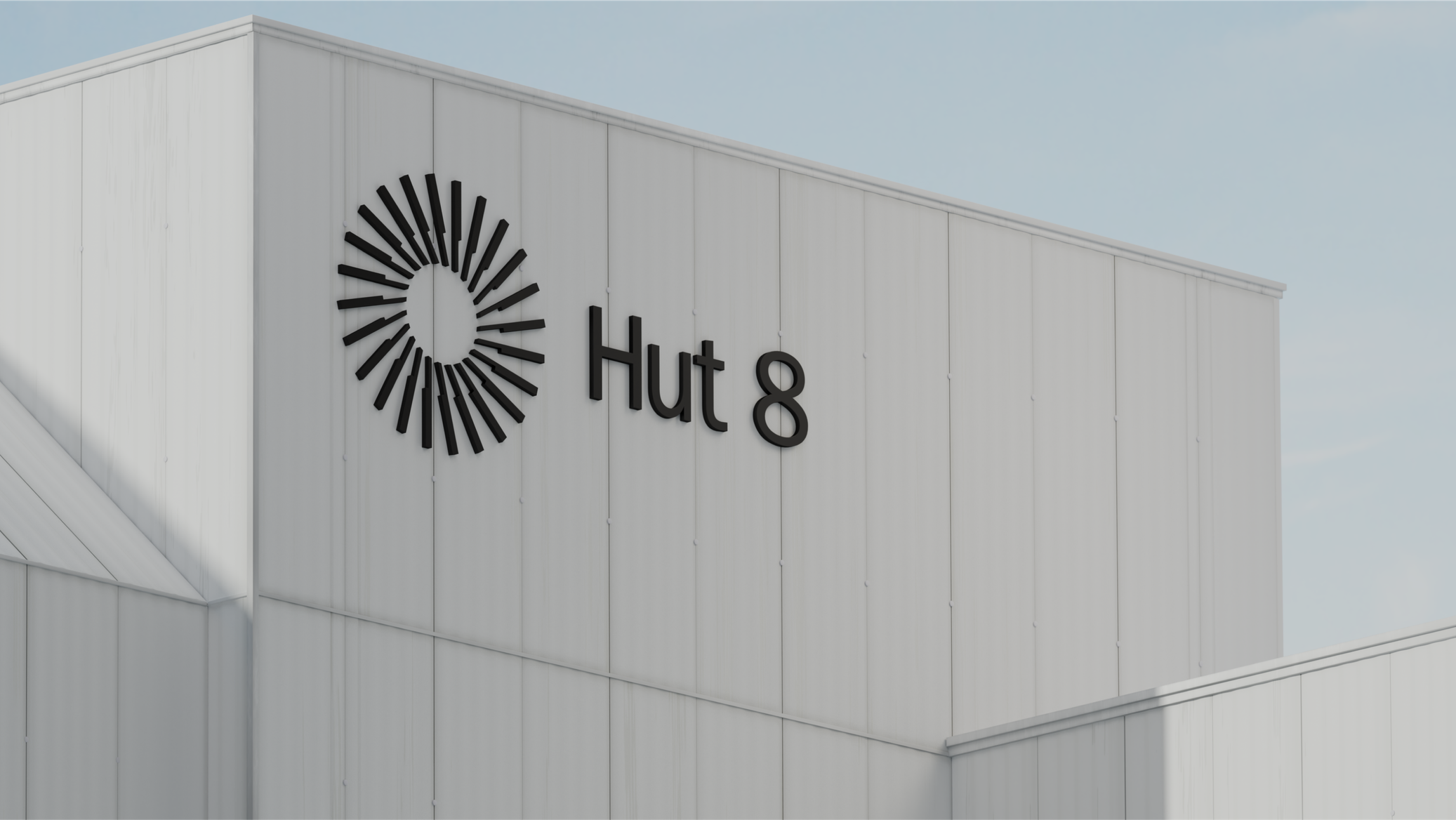 A low-angle exterior shot of a clean, white corrugated-metal industrial building against a clear pale blue sky. Mounted on the upper facade is the "Hut 8" brand signage in black: a circular sunburst/pinwheel logo made of radiating tapered lines beside the wordmark "Hut 8." Soft daylight and gentle shadows give the minimalist, modern structure a crisp, corporate look.