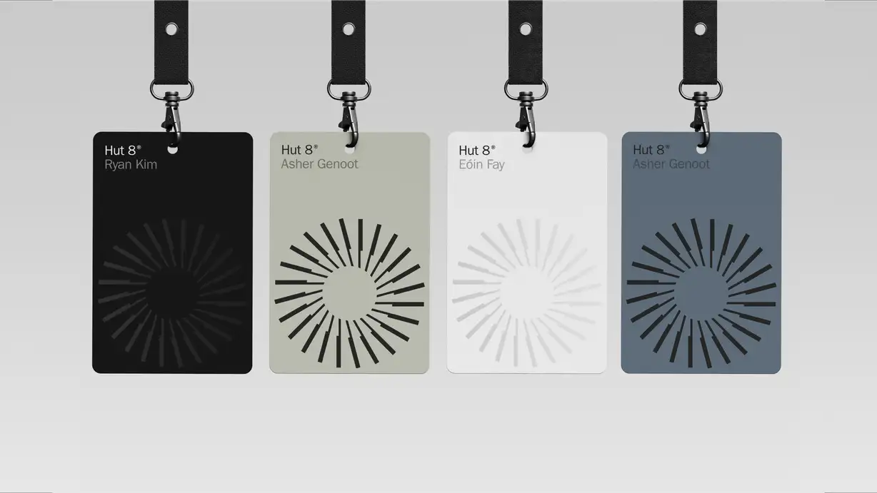 Four Hut 8 ID badges on black lanyards in black, sage green, white, and slate blue, each printed with a name and a circular sunburst logo.