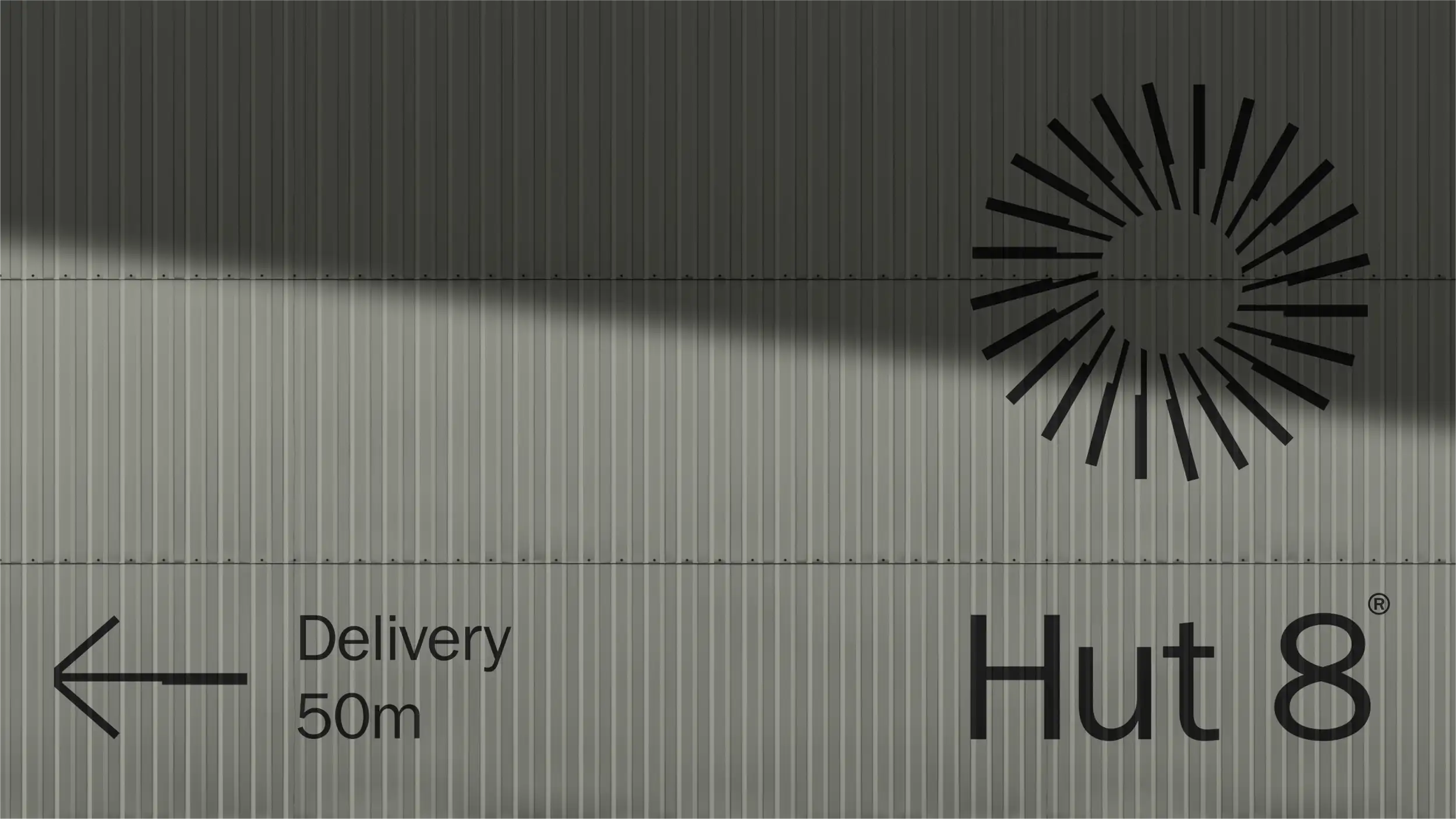 Close-up of a corrugated metal building wall with a black sunburst logo, a "Delivery 50m" directional sign, and the "Hut 8®" wordmark.