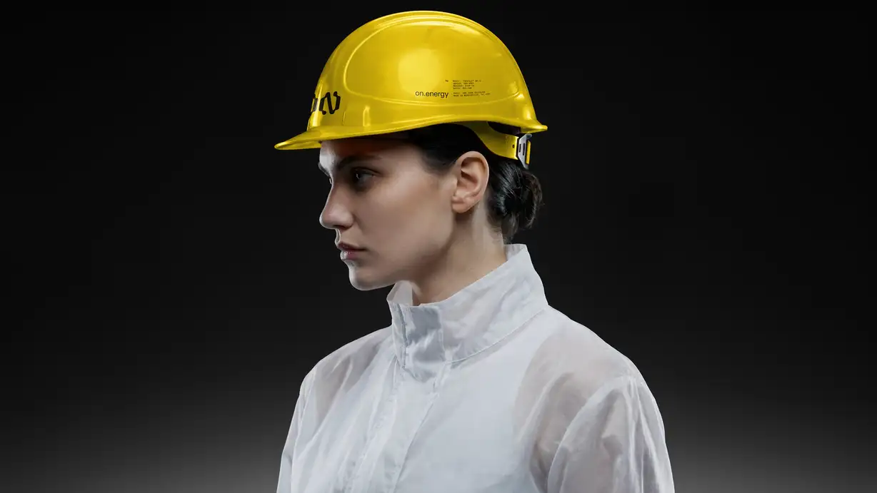 Profile portrait of a woman wearing a glossy yellow hard hat branded with the ON logo and 'on.energy' text, paired with a white technical jacket, against a dark gradient background.