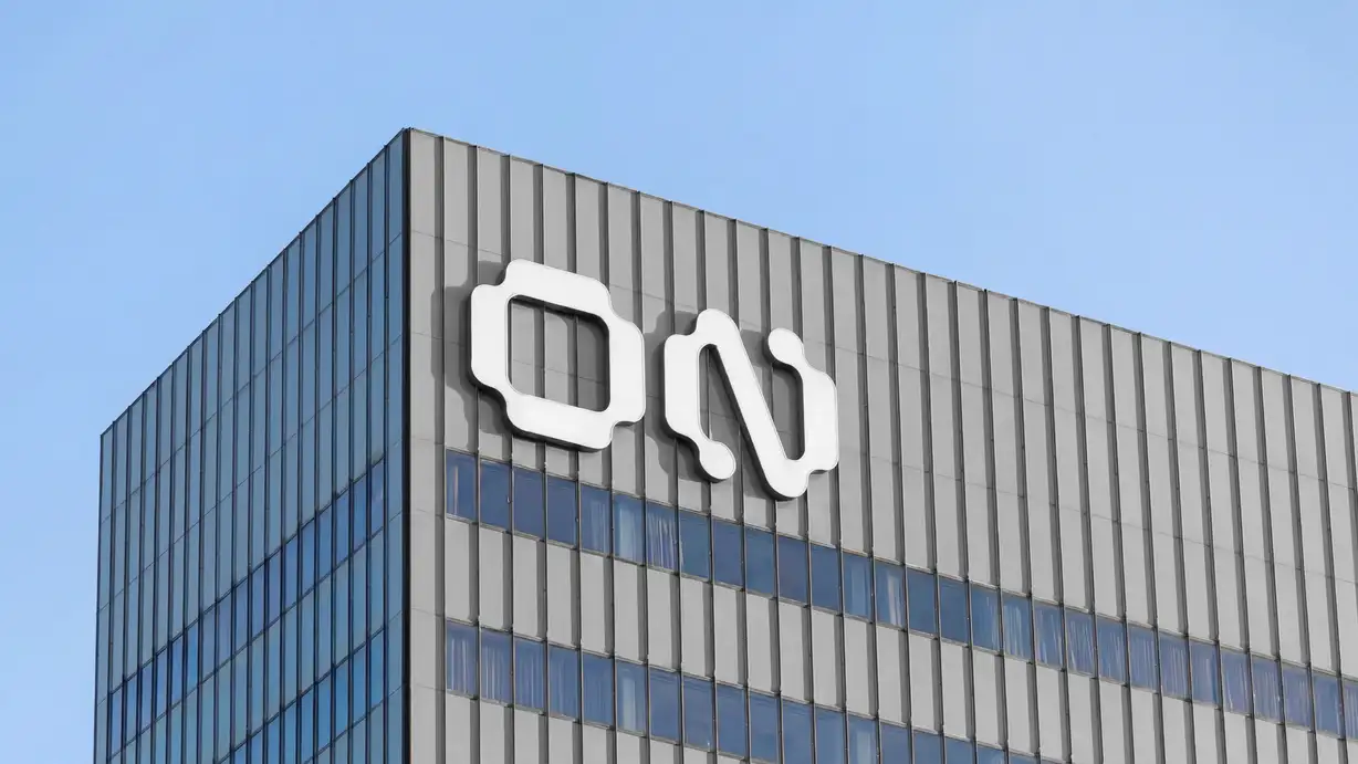 Low-angle photo of a building's corner facade under a blue sky, with the white 'ON' logo mounted on the gray paneled exterior above a glass curtain wall.