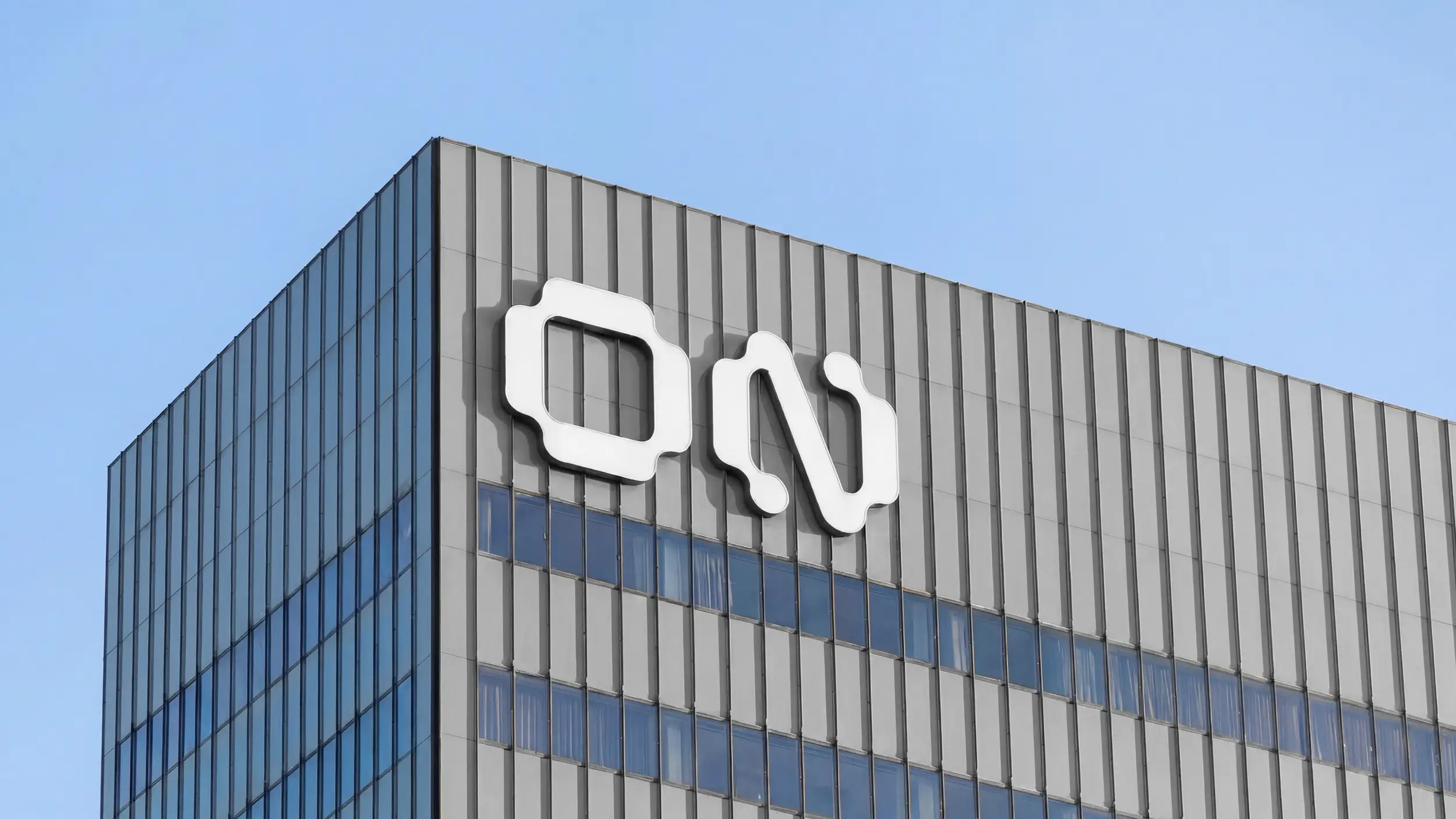 Low-angle photo of a building's corner facade under a blue sky, with the white 'ON' logo mounted on the gray paneled exterior above a glass curtain wall.