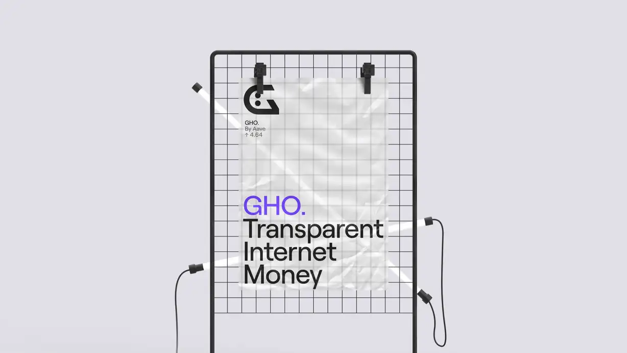A GHO brand poster clipped to a black metal wire-grid display stand against a light lavender-gray background, with two thin white LED tube lights crossing diagonally in front. The slightly crumpled poster is held by two black clips at the top. Its upper-left corner shows the "G" face logo with "GHO. By Aave ↑ 4.64," and the lower half carries the headline "GHO." (in purple) above "Transparent Internet Money" in large black type.