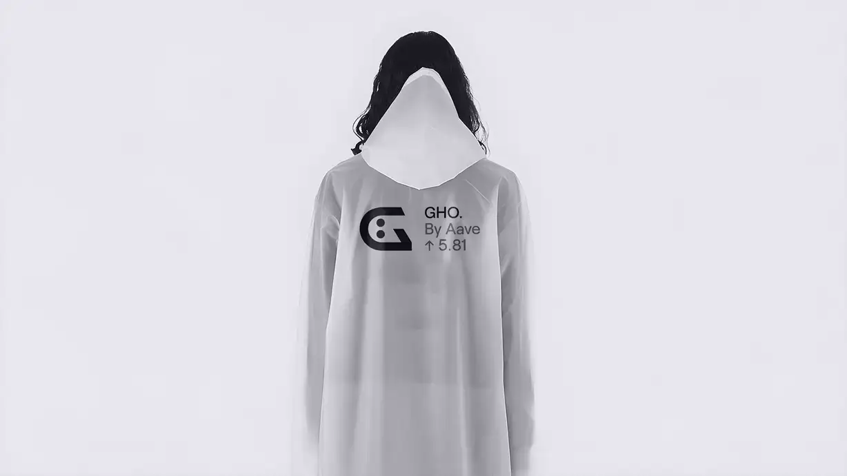 A person stands facing the camera against a plain off-white background, wearing a long, translucent frosted-white hooded raincoat pulled entirely over their head so the face is completely concealed, creating a ghostly, anonymous silhouette. Long dark hair spills out from beneath the hood on both sides. Printed across the chest is a stylized "G" logo (a rounded letter with two dot-like eyes forming a face) beside the text "GHO. By Aave ↑ 5.81." The overall image is nearly monochrome and minimalist.