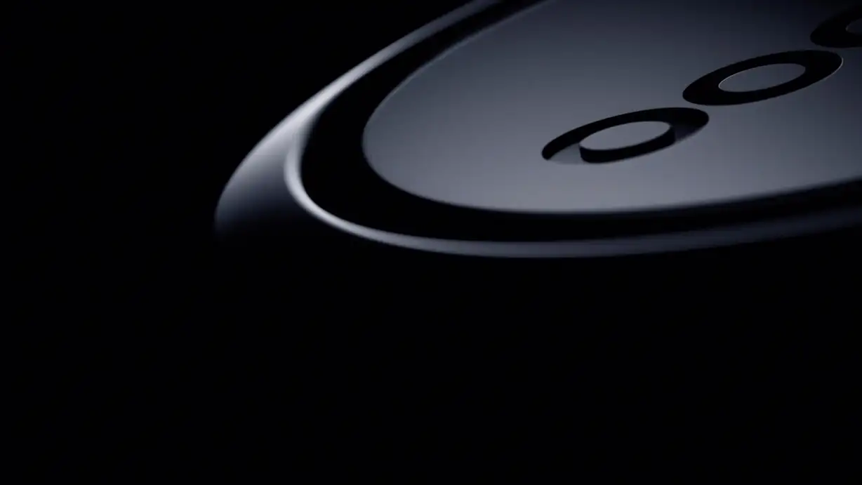 An extreme close-up, dark and moody, of the curved edge of a black circular device showing part of its debossed "OO" logo, mostly lost in shadow.