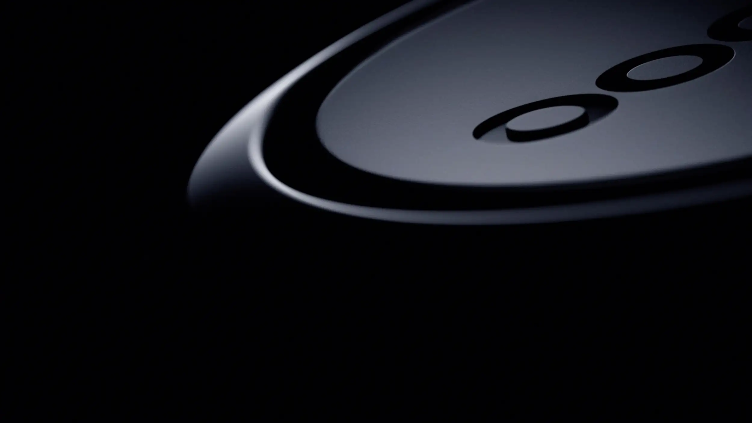 An extreme close-up, dark and moody, of the curved edge of a black circular device showing part of its debossed "OO" logo, mostly lost in shadow.