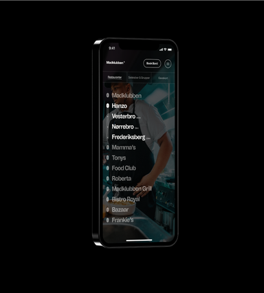 Mockup of a smartphone displaying the Madklubben restaurant app on a black background. The screen shows a dark header with the Madklubben logo, a 'Book Bord' button, and a menu icon, below tabs for Restauranter, Selskaber & Grupper, and Gavekort. A list of restaurant brands is layered over a background photo of a chef in an apron, showing numbered categories (Madklubben with 4 locations, Hanzo with 3, Mamma's, Tonys, Food Club, and Roberta each with 1) and individual Hanzo locations in Vesterbro, Nørrebro, and Frederiksberg with their distances.